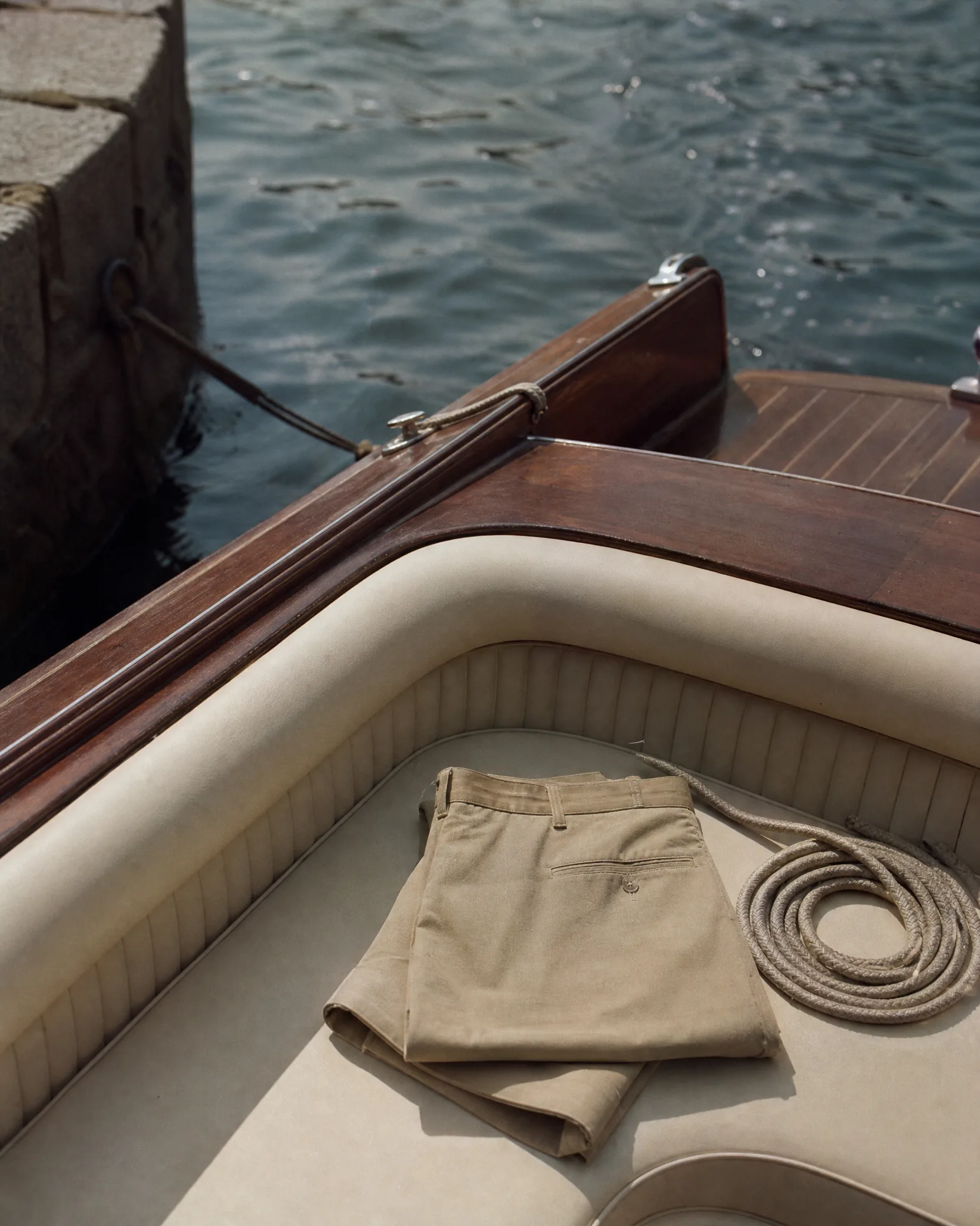 Tan shorts folded on the cream seat of a varnished wooden boat, a coiled rope beside them.