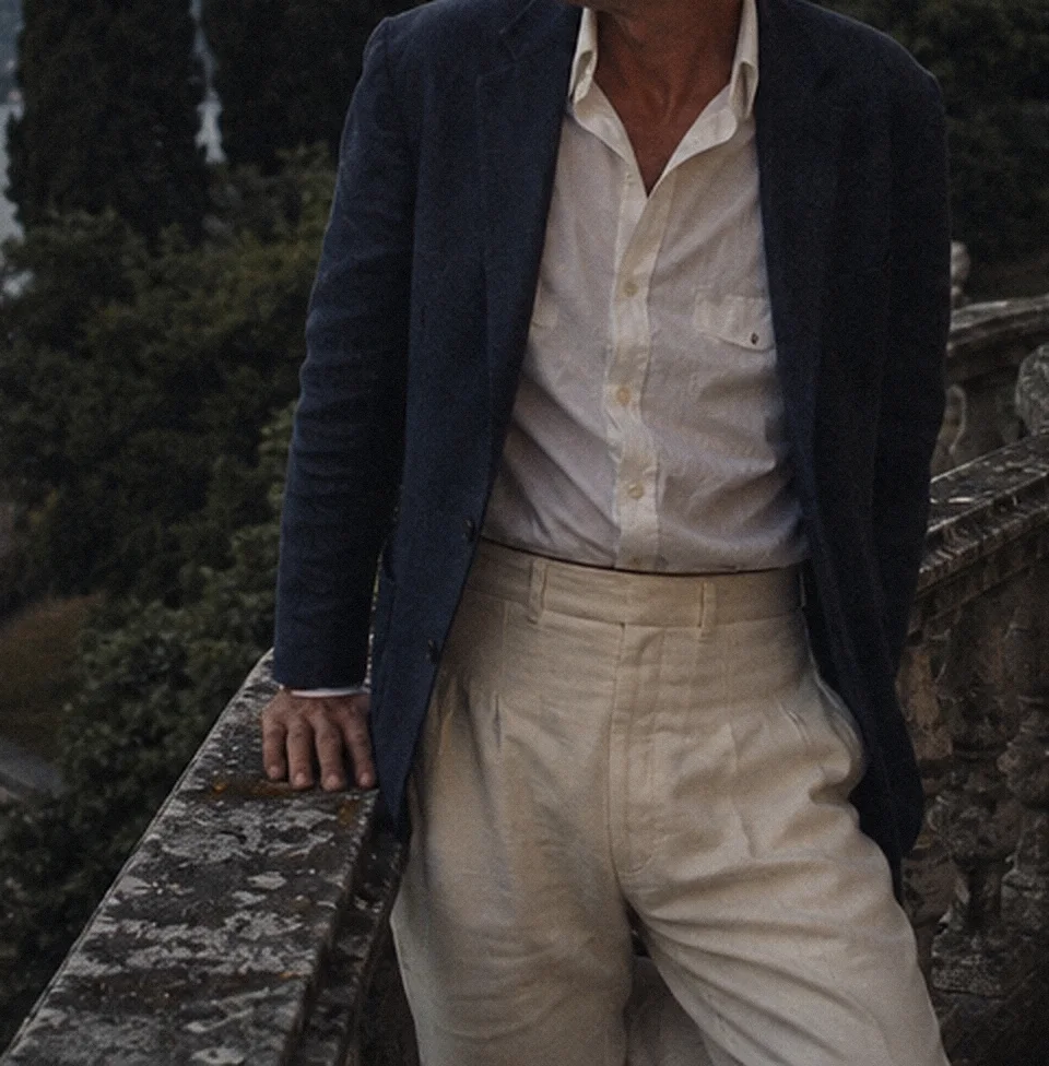 A navy blazer worn open over a white linen shirt and cream trousers, from the collar down.